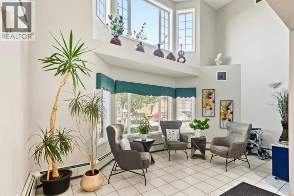 Bright common area with tile floor, tall plants, and grey chairs around tables. - #, 3308 Sienna Park Green Sw, Calgary