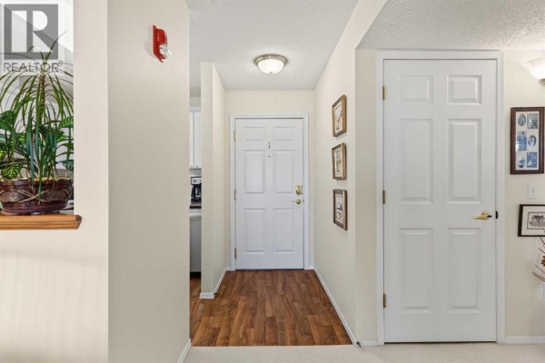 Apartment hallway with wood-look floor, white doors, and decorative framed pictures. - #, 3308 Sienna Park Green Sw, Calgary