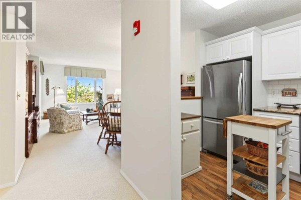 View from apartment hallway showing a dining area and kitchen with stainless steel appliances. - #, 3308 Sienna Park Green Sw, Calgary