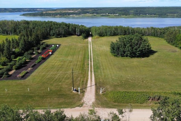 Aerial view of a long gravel driveway leading to the mobile home with a treed area and river. - , Lake Of The Prairies