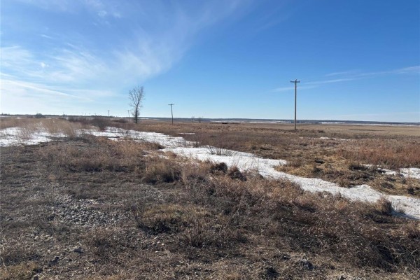 Rural landscape with dry vegetation, melting snow patches, and utility poles against a bright blue sky. - 39800 Main Street, Nesbitt