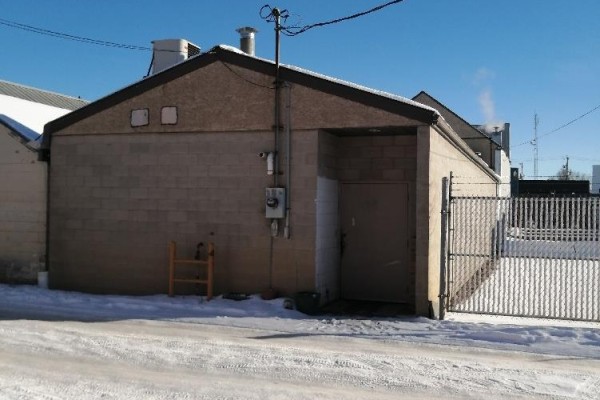 Rear exterior of a light brown brick building with a metal door and chain-link fence. - , Provost