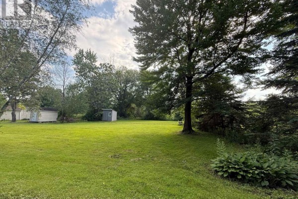A sunny, grassy field bordered by trees, with two utility sheds visible. - 0 153rd Avenue, South Glengarry