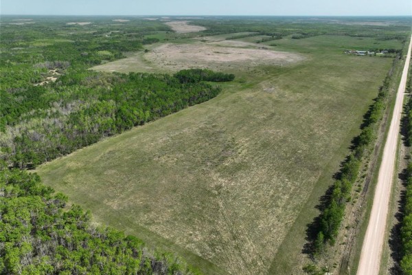 Aerial view of a vast open field bordered by dense green trees and a dirt road. - 0 3w Road, Inwood