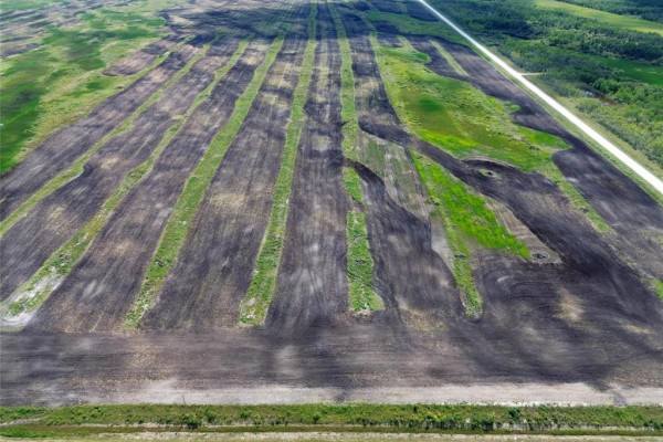 Overhead view of a partially tilled field featuring dark soil rows and vibrant green grass. - 0 481 Road, Ste Rose Du Lac