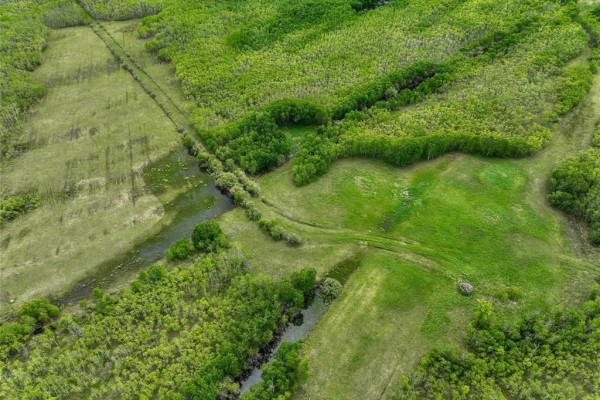 Top-down view of a rural landscape featuring forested areas, grassy clearings, and a small creek. - 0 68 Highway, Siglunes Rm