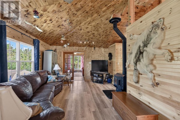 Living room with a brown leather sectional sofa, wood-paneled walls and ceiling, and a wood stove. - 0 Dam Pond Road, Brigus Junction