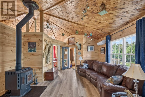 Living room with a large curved leather sofa, wood-paneled walls, and windows overlooking greenery. - 0 Dam Pond Road, Brigus Junction