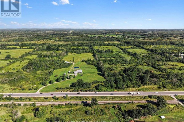 Aerial view of a large parcel of land with a house and pond, bordered by a highway and fields. - 0 Highway 7, Tay Valley