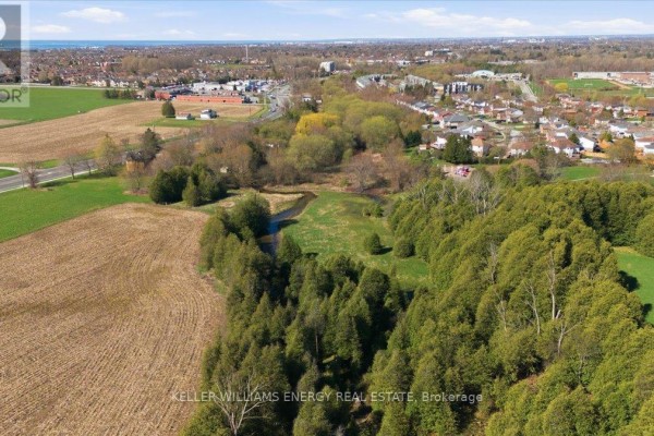 Wide aerial shot showing a vast green field adjacent to a suburban neighborhood and a highway interchange. - 0 Nash Road, Clarington