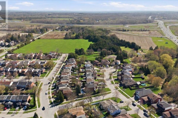Sunlit green field with mature trees in the foreground and residential homes in the background. - 0 Nash Road, Clarington