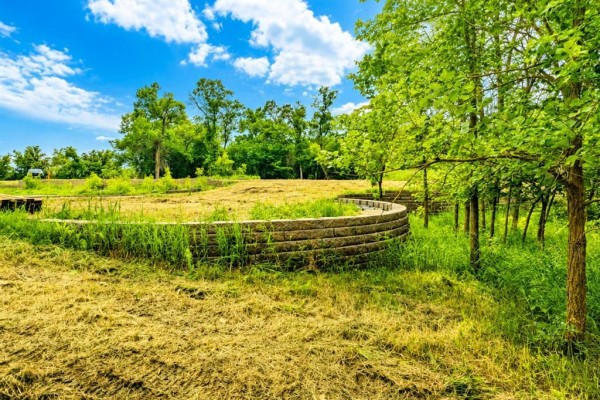 A retaining wall made of stacked stone blocks curves around a grassy area with scattered trees. - 0 Old Bog Road, Lorette