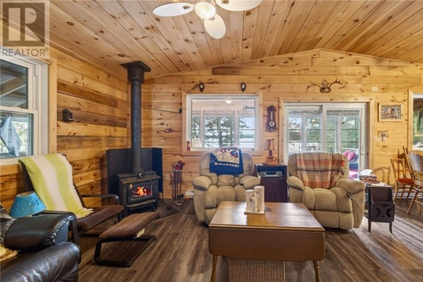 Living room with a wood stove, two recliners, a sofa, and wood paneling. - 0 Panache Lake, Espanola