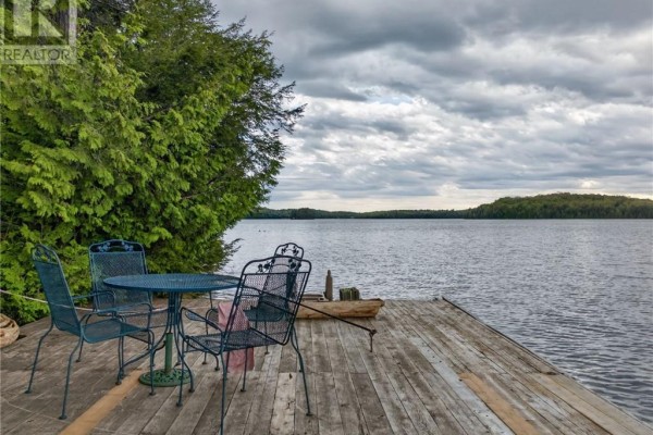 Dock with metal chairs and table overlooking a wide lake and tree-lined shore. - 0 Panache Lake, Espanola