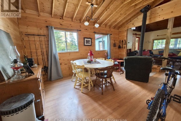 Living and dining area with wooden walls, round table, fireplace, and fishing rods. - 0 Rock Lake Road, Algonquin Highlands
