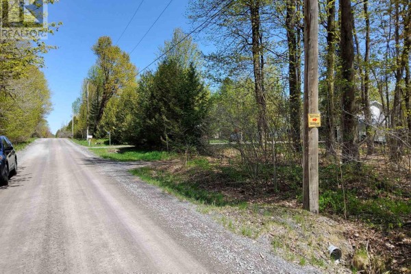 View of the dirt road with trees on either side and a property boundary sign. - 0 Totem Ranch Road, Edwardsburgh/cardinal