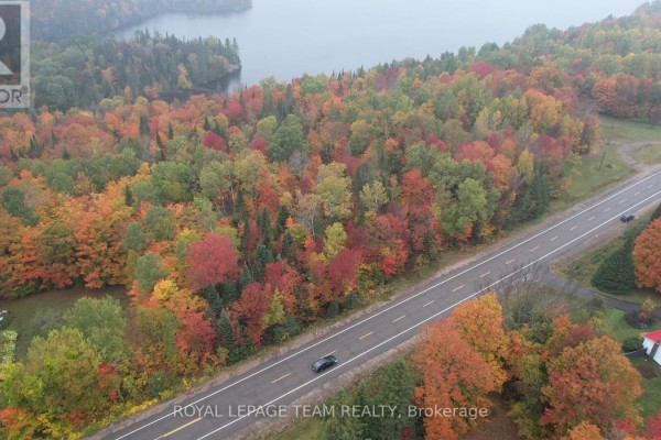 Aerial view of a highway passing through dense forest with colorful autumn trees and a distant lake. - 00 62 Highway, Hastings Highlands