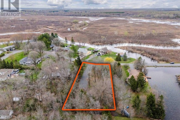 Aerial view of a residential area showing a wooded lot outlined in orange, with water and marshland in the background. - 0000 Tree Haven Road, South Glengarry