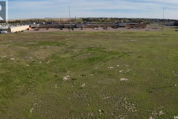 Aerial view of a large commercial building with a parking lot and a vacant green field. - 01 Springs Drive, Swift Current