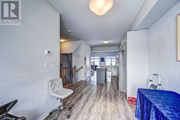 Interior hallway with light grey walls, wood-look flooring, staircase, kitchen island, and storage units. - 03 - 314 Equestrian Way, Cambridge