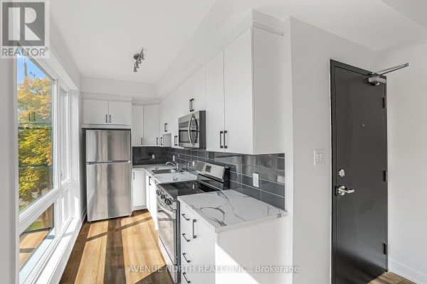Compact kitchen with white cabinets, stainless steel appliances, gray tile backsplash, and marble countertop. - 03 - 391 Dieppe Street, Ottawa