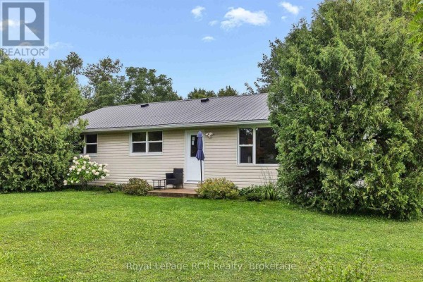 Front view of a light-colored bungalow with a dark metal roof, featuring a white door and two chairs. - 046285 Old Mail Road, Meaford