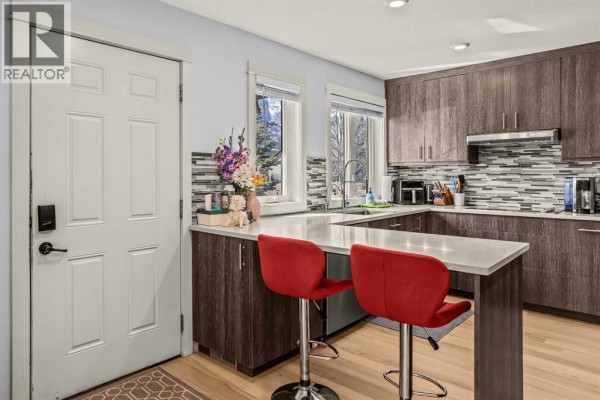 Kitchen with U-shaped counter, stainless steel dishwasher, and wood cabinetry with silver hardware. - 1, 1406 2nd Avenue, Canmore