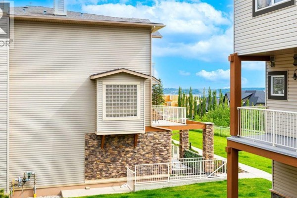 Covered patio with stone pillars, outdoor furniture, and a view of a green lawn. - 1, 169 Rockyledge View Nw, Calgary