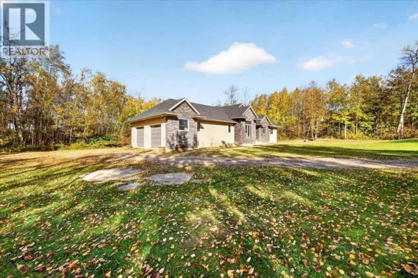 Side exterior view of the beige bungalow showcasing a three-car attached garage with grey doors. - 1, 20120 Twp Rd 515 Road, Rural Beaver County