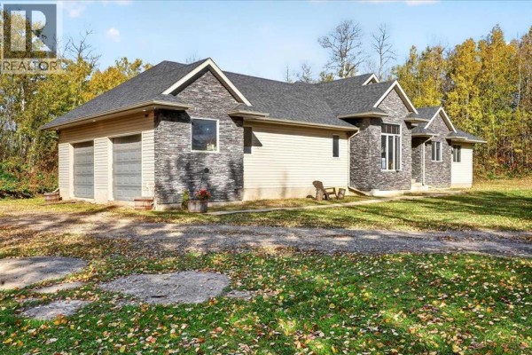 Close-up side view of the beige bungalow's exterior, highlighting stone accents and a triple garage. - 1, 20120 Twp Rd 515 Road, Rural Beaver County