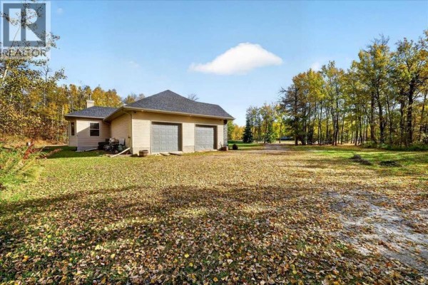 Rear-side view of the bungalow with a treed backdrop and a spacious lawn covered in fallen leaves. - 1, 20120 Twp Rd 515 Road, Rural Beaver County