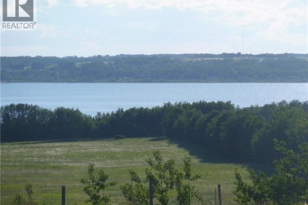 A wide blue lake bordered by dark green trees and fields under a hazy sky. - 1, 420069 Range Road 284, Rural Ponoka County