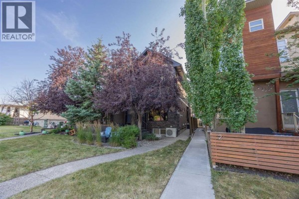 Small patio with two blue chairs, coffee table, and surrounding plants. - 1, 4711 17 Avenue Nw, Calgary