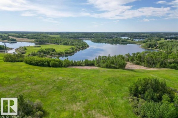 Wide aerial view of green, grassy fields and treed areas sloping towards a calm lake. - 1, 52313 Twp Rd 24, Rural Parkland County