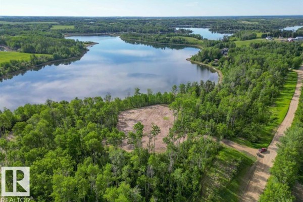 Aerial view of a cleared patch of land surrounded by dense green trees next to a lake. - 1, 52313 Twp Rd 24, Rural Parkland County
