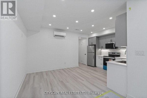 View of a basement living area with light laminate flooring and a modern grey kitchen. - 1 (bsmt) - 591 Oakwood Avenue, Toronto
