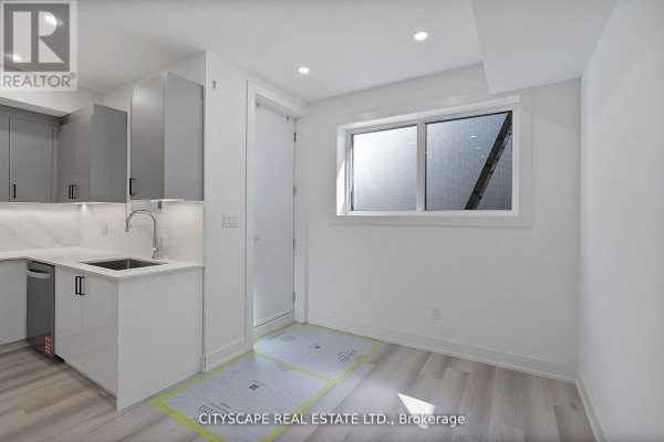 Kitchenette with white and grey cabinetry, stainless steel appliances, and a window with frosted glass. - 1 (bsmt) - 591 Oakwood Avenue, Toronto