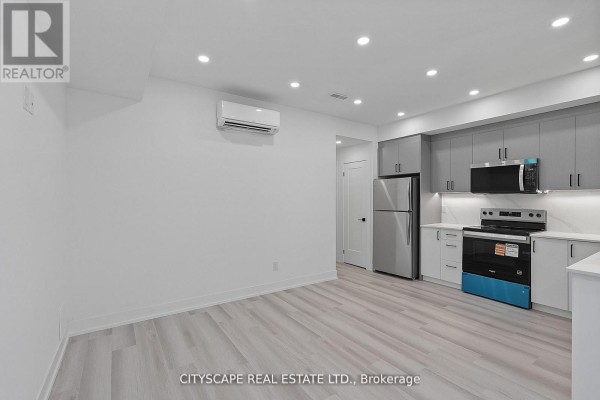 Basement studio apartment with grey kitchen, stainless steel fridge, and air conditioning unit. - 1 (bsmt) - 591 Oakwood Avenue, Toronto