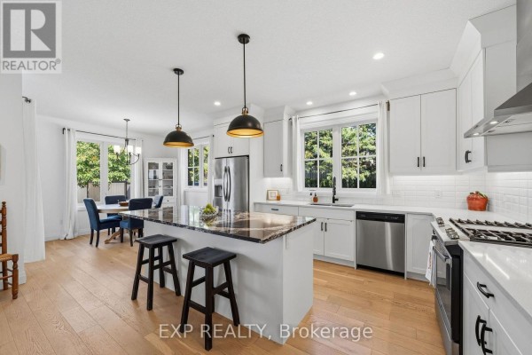 White kitchen with island, dark granite counters, stainless steel appliances, and dining area. - 1 - 10038 Oxbow Drive, Middlesex Centre