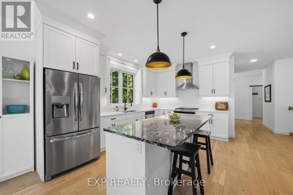 Modern white kitchen with stainless steel refrigerator, island, and pendant lighting. - 1 - 10038 Oxbow Drive, Middlesex Centre