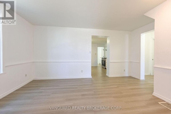 Living room with white walls, wainscoting, and laminate flooring, showing an opening to the kitchen. - 1 - 103 Mulcaster Street, Barrie