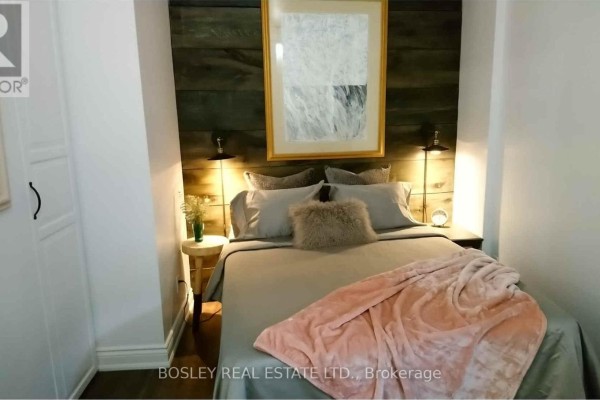 Bedroom with a queen-sized bed, wood accent wall, and bedside lamps. - 1 - 11 Boustead Avenue, Toronto