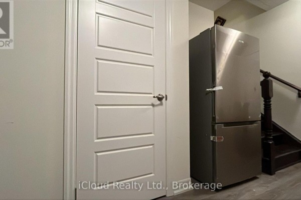 Stainless steel refrigerator next to a white paneled door and wooden staircase. - 1 - 141 Marvin Avenue, Oakville