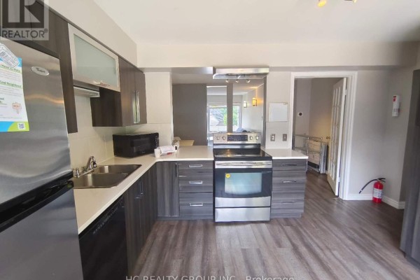 Modern kitchen with dark grey cabinets, stainless steel appliances, and a view into living area. - 1 - 1548 Richmond Street, London North