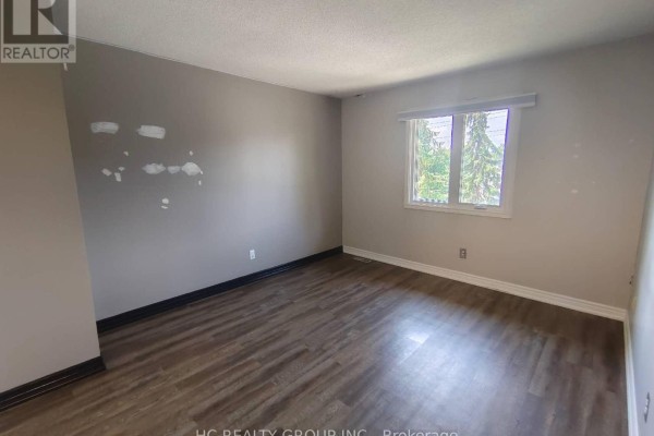 Empty bedroom with light grey walls, a window overlooking trees, and wood-look flooring. - 1 - 1548 Richmond Street, London North