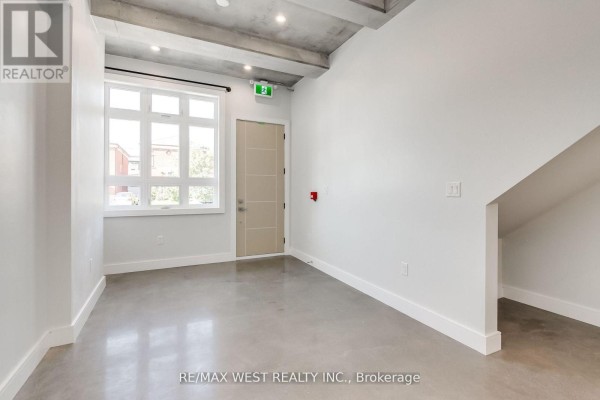 Open doorway view into a bright, modern living area with a white kitchen and grey floor. - 1 - 1745 Keele Street, Toronto