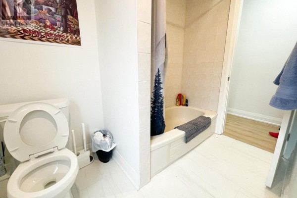 Small bathroom with a toilet, bathtub with shower curtain, and tiled floor. - 1 - 20 Sullivan Street, Toronto