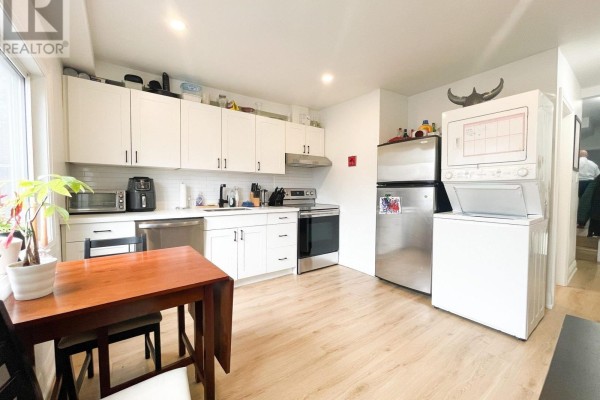 Bright white kitchen with stainless steel appliances, wood-look flooring, and a dining table. - 1 - 20 Sullivan Street, Toronto