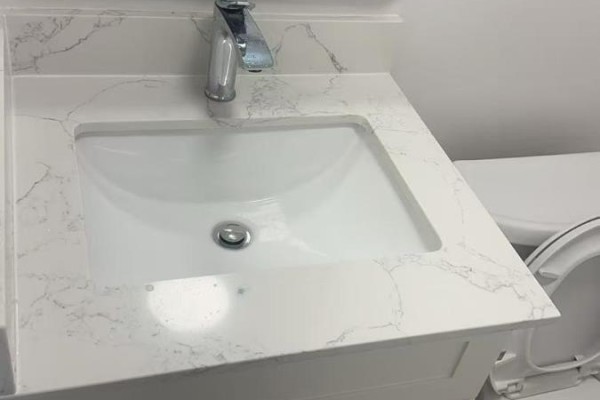 Close-up of a white sink with a chrome faucet set in a white countertop with marble veining. - 1 - 202 O'connor Drive, Toronto