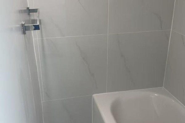 Bathroom with a white bathtub and light gray tiled walls. - 1 - 202 O'connor Drive, Toronto
